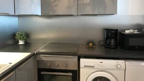 A compact kitchen with a washing machine, a microwave, and a small plant on the counter. - T2 , 50m² Avec vue mer à Carnon Plage (Mauguio)