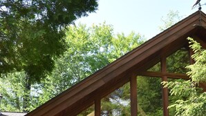 A wooden cabin with a deck, large windows, and outdoor seating. - Luxurious Waterfront with Mountain Views (Tupper Lake)