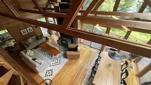 A spacious living area with a fireplace, a dining table with chairs, and a large window offering a view of the outdoors. - Luxurious Waterfront with Mountain Views (Tupper Lake)