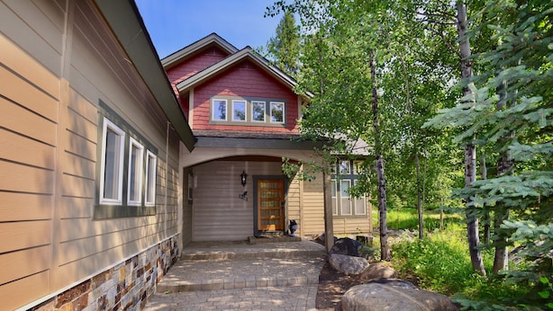 A two-story house with a brick pathway leading to the front door, surrounded by trees and large rocks. - Hart of McCall - Mountain retreat with hot tub and sauna near downtown and golf (McCall)