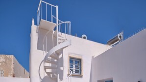 A white building with a spiral staircase, a blue door, and a small outdoor seating area. - Happy Retreat Paros (Paros)