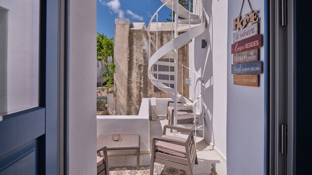 A spiral staircase leading to a balcony with a table and chairs, a view of the sky, and a wall with wooden signs. - Happy Retreat Paros (Paros)