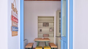 A room with a wooden floor, a table with benches, a bookshelf, and a welcome sign. - Happy Retreat Paros (Paros)