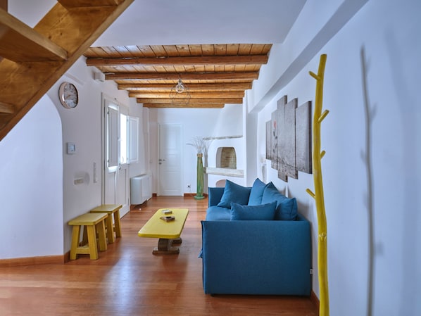 A spacious living room with a wooden ceiling, a blue sofa, a yellow table, and a wooden bench.