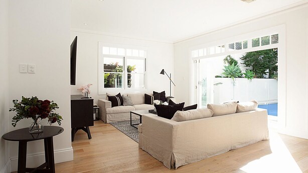 A modern living room with a beige sofa, a coffee table, and a side table with a vase. There is a window with a view of greenery outside. - Palatial Home w/ courtyard,private garden,pool,central -yet peaceful location (Rose Bay)