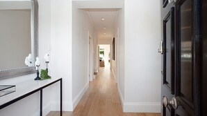 A hallway with a wooden floor, white walls, a black door, and a mirror on the left. - Palatial Home w/ courtyard,private garden,pool,central -yet peaceful location (Rose Bay)