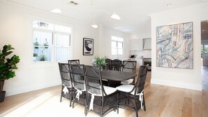 A dining area with a dark wooden table and black wicker chairs, a large abstract painting on the wall, and a view of the kitchen through an open door. - Palatial Home w/ courtyard,private garden,pool,central -yet peaceful location (Rose Bay)