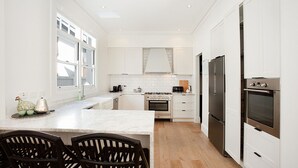 A modern kitchen with white cabinetry, a marble countertop, a built-in oven, a refrigerator, and a dining area with two chairs. - Palatial Home w/ courtyard,private garden,pool,central -yet peaceful location (Rose Bay)