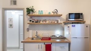 Eine Küche mit Mikrowelle, Kühlschrank, Spüle und Holzregalen mit Küchenutensilien.