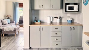 Una cocina compacta con armarios grises, un microondas y una cafetera. Hay un comedor con un sofá y una silla.