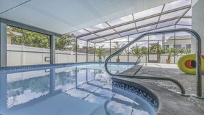 Una piscina interior con paredes de vidrio transparente, borde de azulejos y escalera de metal.