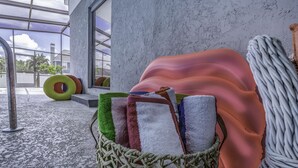 Una habitación con un ventanal grande, una cesta de mimbre con toallas y una zona junto a la piscina con una silla de descanso y flotadores.
