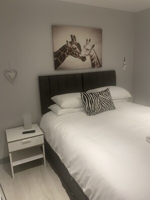 Une chambre à coucher avec un lit, une table de chevet, une télécommande et une décoration en forme de cœur accrochée au mur.