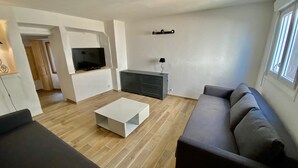 A modern living room with a flat-screen TV, a grey sofa, and a white coffee table. - At the foot of Mont Ventoux<br>Village center<br>Fully renovated apartment<br> (Malaucène)