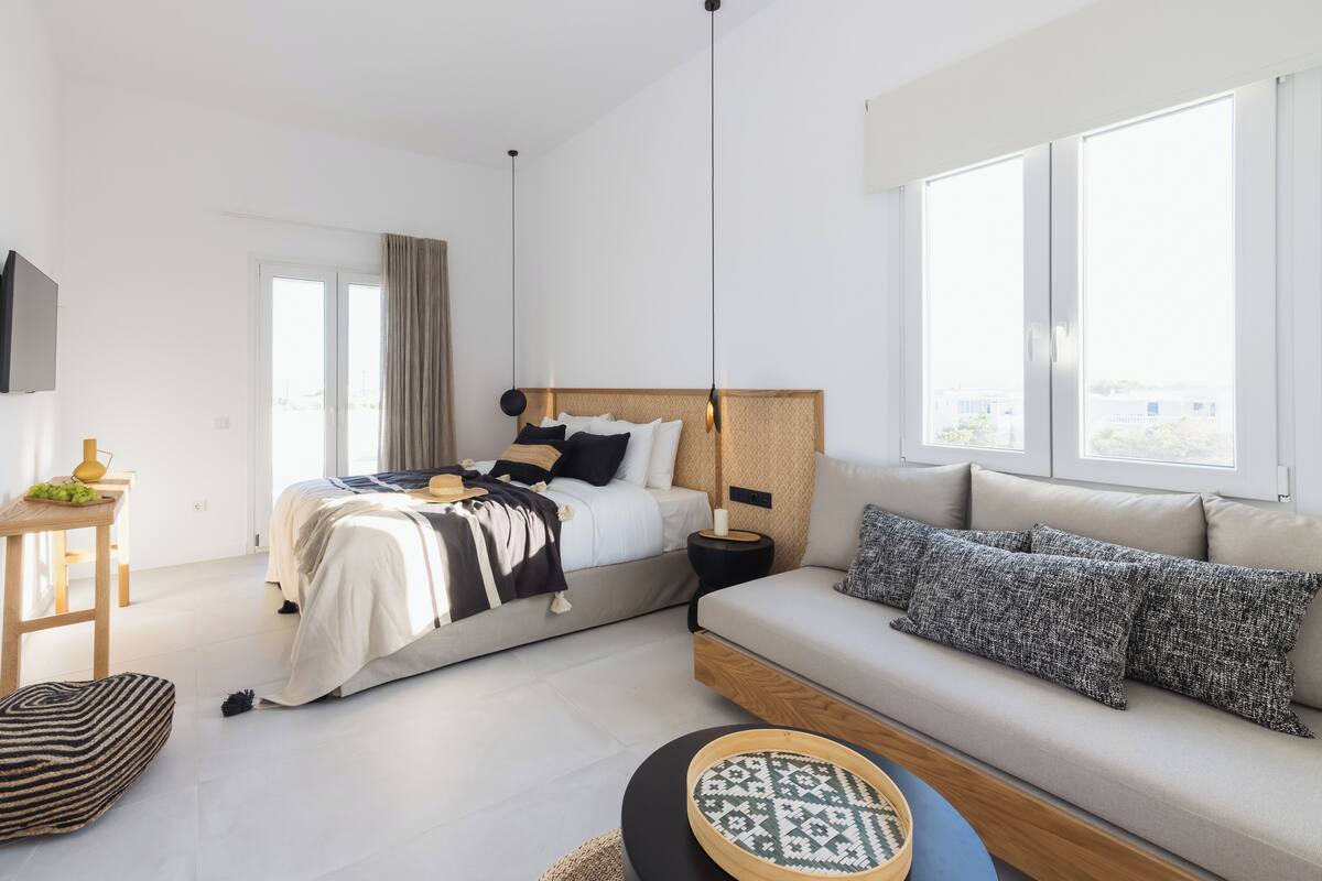 A modern bedroom with a bed, a sofa, a TV, and a large window.