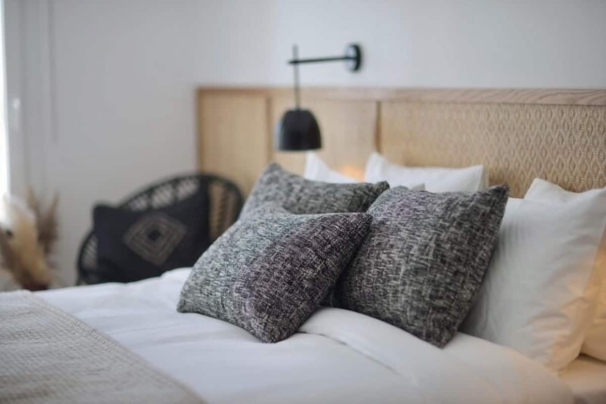 A neatly made bed with grey and white pillows, a black wall-mounted lamp, and a wooden headboard.