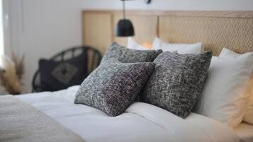 Una cama bien hecha con almohadas grises y blancas, una lámpara negra fijada a la pared y un cabecero de madera.