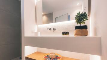Un baño moderno con un tocador de madera, un espejo redondo, una planta en maceta y un estante con artículos de aseo.