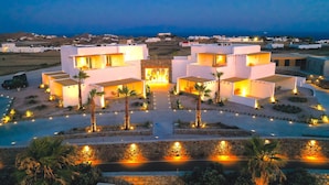 Een modern resort met meerdere witte gebouwen, een zwembad en palmbomen.