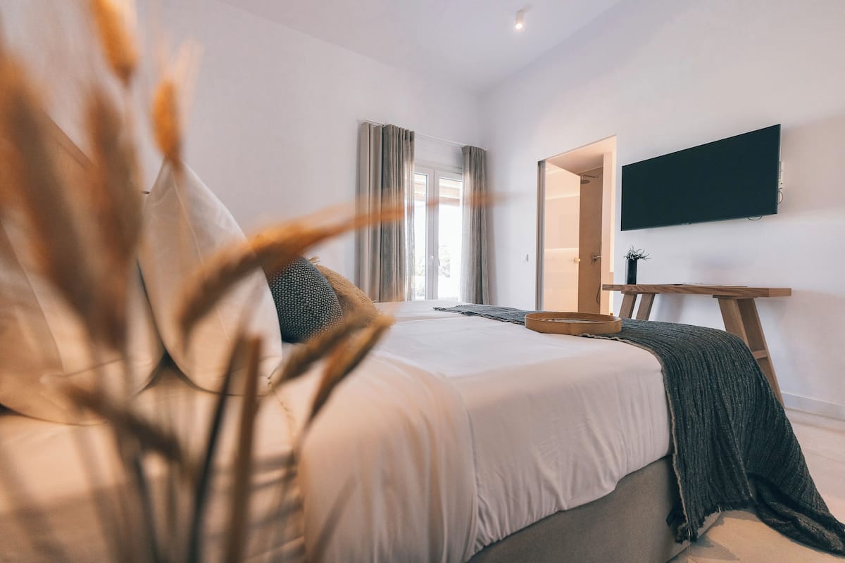 A modern bedroom with a large bed, a flat-screen TV mounted on the wall, and a wooden side table.