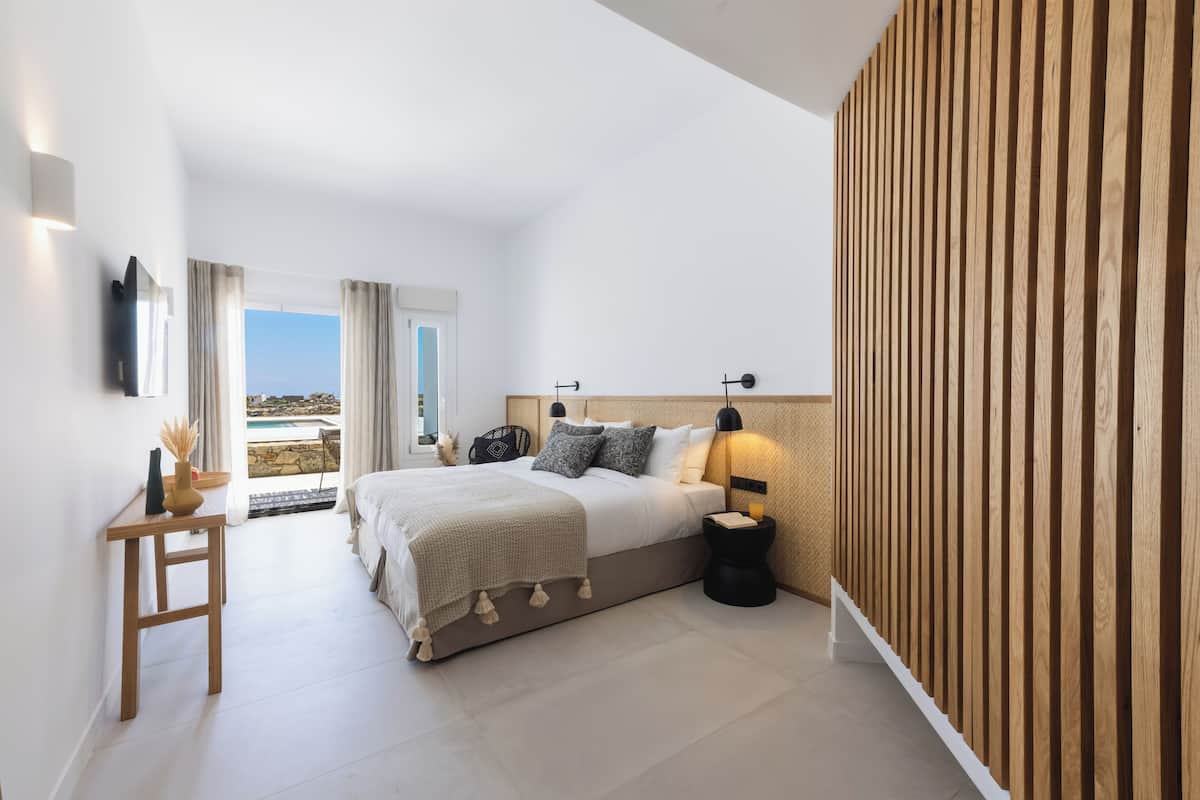 A modern bedroom with a large bed, a bedside table, a nightstand, and a view of the outdoors.