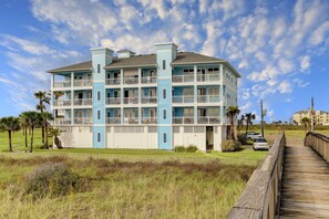 A multi-story hotel with balconies, a wooden boardwalk, and a grassy area with palm trees. - Pointe West Top Floor Renovated Spacious Beachfront 3/3 Resort Condo (Galveston)