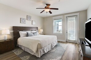 A bedroom with a large bed, a ceiling fan, a nightstand with a lamp, a dresser, and a television. - Pointe West Top Floor Renovated Spacious Beachfront 3/3 Resort Condo (Galveston)