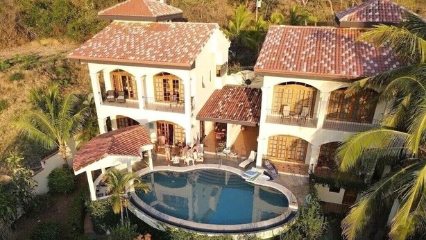 Une grande maison avec une piscine, entourée d’une végétation luxuriante et de palmiers.