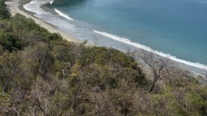 Un paysage côtier avec une plage, une eau d’un bleu limpide et des collines à l’horizon.
