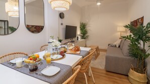 Ein modernes Wohnzimmer mit Essbereich, ausgestattet mit Korbmöbeln, einem Flachbildfernseher und einem großen Spiegel.
