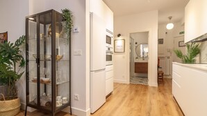 Eine moderne Küche mit weißen Schränken, einem Kühlschrank und einer Mikrowelle. Ein Glastischschrank beherbergt Dekoration und einen Topfpflanzen.
