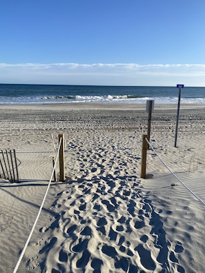 Une plage de sable où l’on peut voir des empreintes de pas menant à l’eau, une clôture en bois et un panneau bleu portant le numéro 8900.