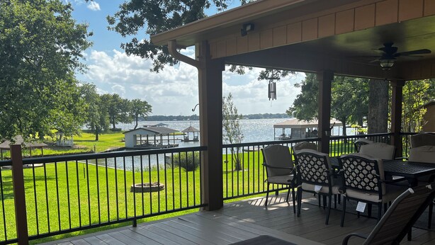 A covered outdoor area with a view of a lake, featuring a deck with chairs and tables, a fenced lawn, and a gazebo. - Fisherman’s Getaway with Sunset Views & Room for 11 (Jewett)