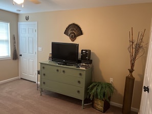 A room with a television on a dresser, a decorative wall piece, a door, and a plant. - Fisherman’s Getaway with Sunset Views & Room for 11 (Jewett)