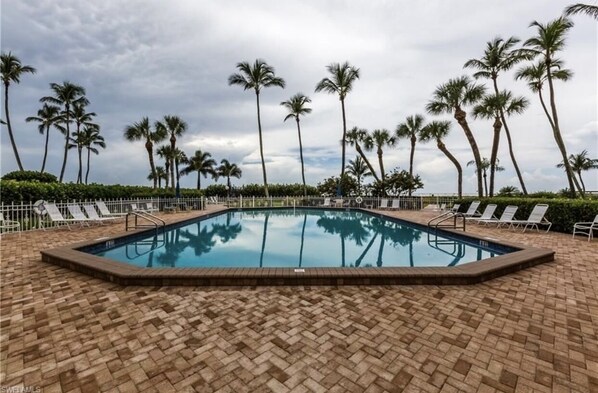 A rectangular pool with a brick border, surrounded by white lounge chairs and palm trees. - Beachfront Bliss - Where comfort meets the Coast (Marco Island)