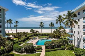 A pool area with a view of the beach, surrounded by palm trees and a clear sky.