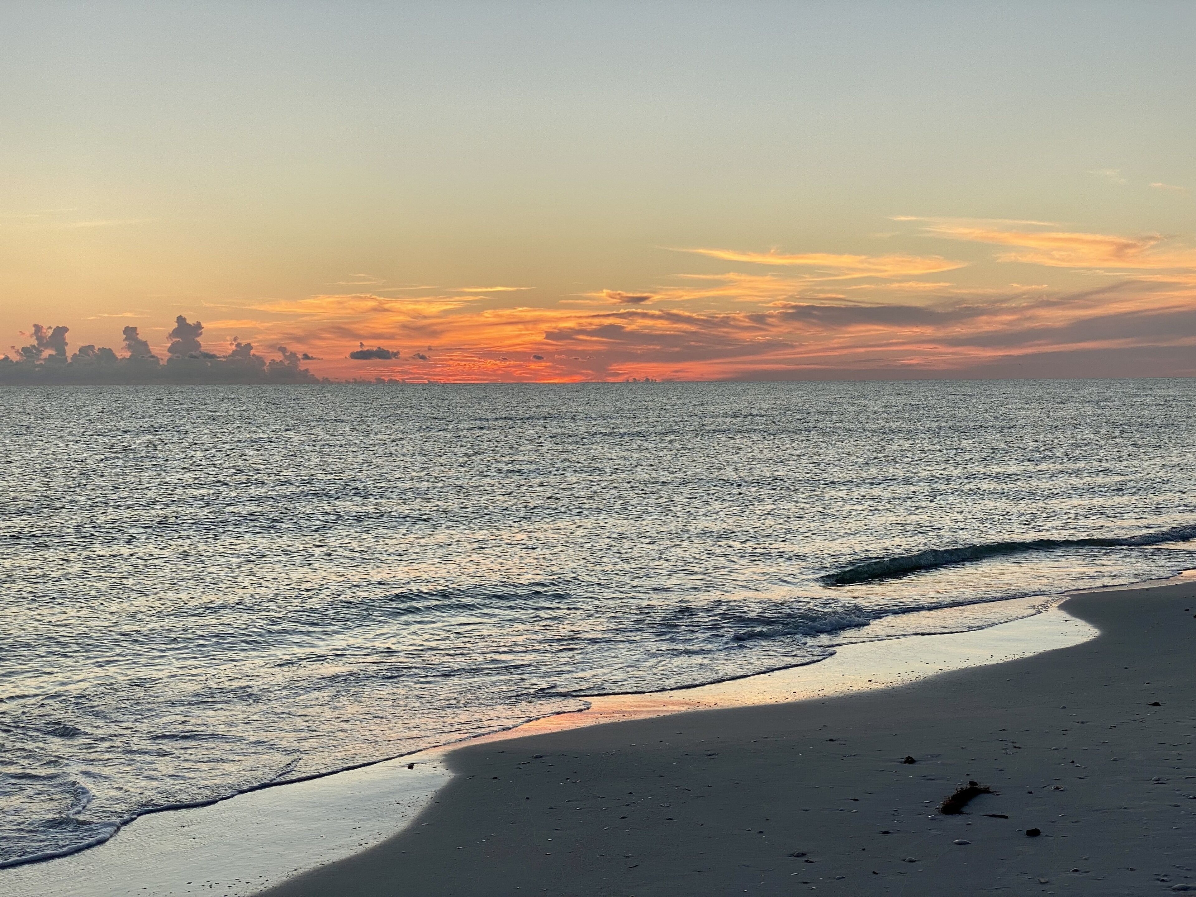 A beach with a calm sea and a sunset.