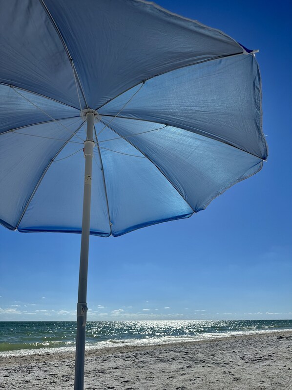 A beach umbrella with a clear view of the ocean and sandy beach in the background.