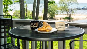 Una mesa redonda con un croissant y dos tazas en un balcón con vista al agua.