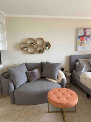 Un salon moderne avec un canapé gris, un pouf rond et une étagère murale hexagonale agrémentée de plantes.