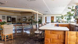 A spacious lobby with a marble floor, a central island with bar stools, and a seating area with wicker chairs. - Minutes to Beach | Pool+Gym | WFH Station | Lanai (Honolulu)