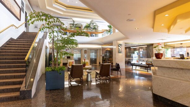 A hotel lobby with a staircase, seating area, reception desk, and a large indoor plant. - Minutes to Beach | Pool+Gym | WFH Station | Lanai (Honolulu)