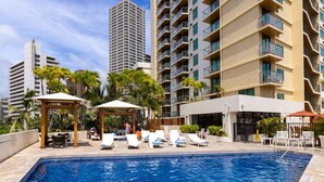 A swimming pool with lounge chairs, a gazebo, and a building with balconies. - Minutes to Beach | Pool+Gym | WFH Station | Lanai (Honolulu)