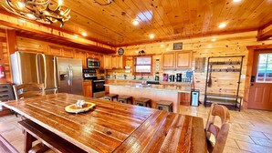 A spacious wooden cabin interior with a large dining table, kitchen area, and a cozy fireplace. - NEW LISTING-IN-Cabin Pool-Arcades-King Beds (Sevierville)