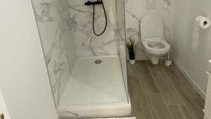 Moderni kylpyhuone, jossa on lasiseinällä varustettu suihku, wc ja pieni ruukkukasvi.