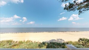 A beach view from a balcony with a railing, clear sky, and distant shoreline. - Ocean Cottage 56 The Cottages at Jekyll Island Oceanfront (Jekyll Island)