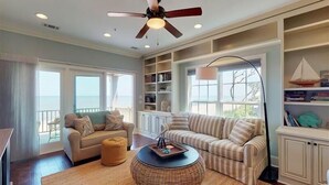 A living room with a ceiling fan, two sofas, a round coffee table, and a bookshelf. - Ocean Cottage 56 The Cottages at Jekyll Island Oceanfront (Jekyll Island)
