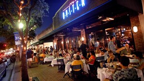 An outdoor dining area with tables and chairs, a brick building with a neon sign, and trees with string lights. - Beautiful remodeled condo. Steps away from area's top nightlife/1 mi. from beach (Delray Beach)