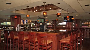 A bar with wooden chairs, a bar counter, and a television screen.