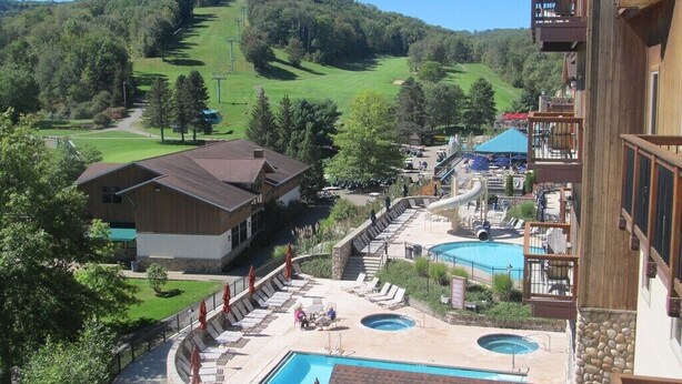 A resort with a pool area, a ski slope in the background, and a building with a balcony.